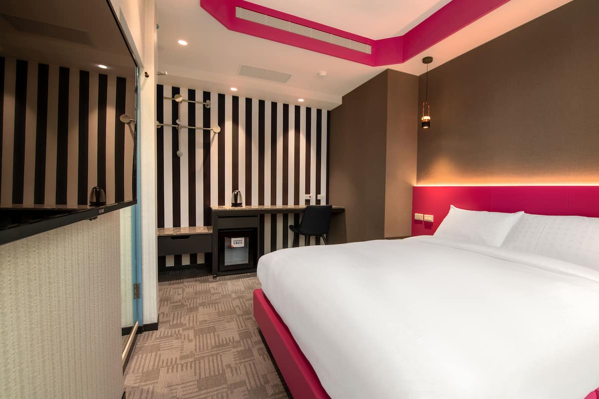 A hotel room with a large bed, a desk, and a chair. There is a striped wall and a red accent wall.