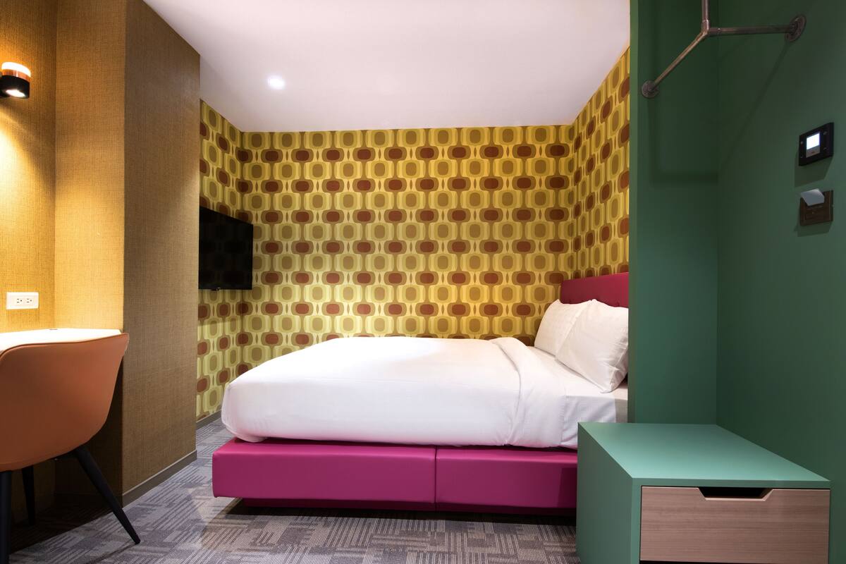 A modern hotel room with a bed, a desk, and a TV.