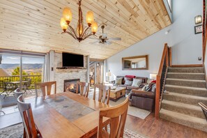 A spacious living area with a large wooden dining table, comfortable seating, a fireplace, and a view of the outdoors. - Pool & Hot Tub | Deck with Views | Large Kitchen (Steamboat Springs)