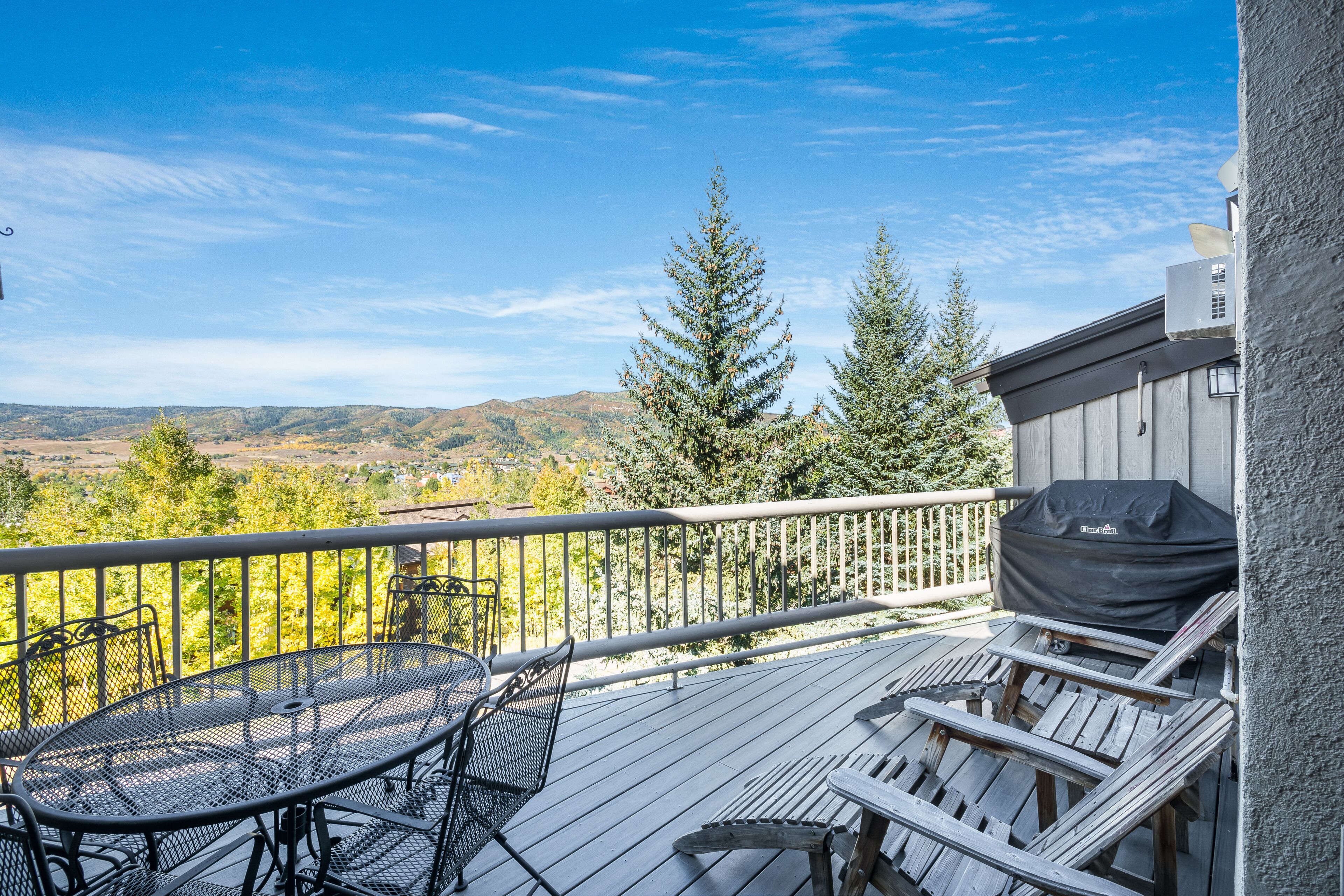 Une terrasse dotée d’une table et de chaises, offrant une vue panoramique sur un paysage pittoresque avec des collines et des arbres.