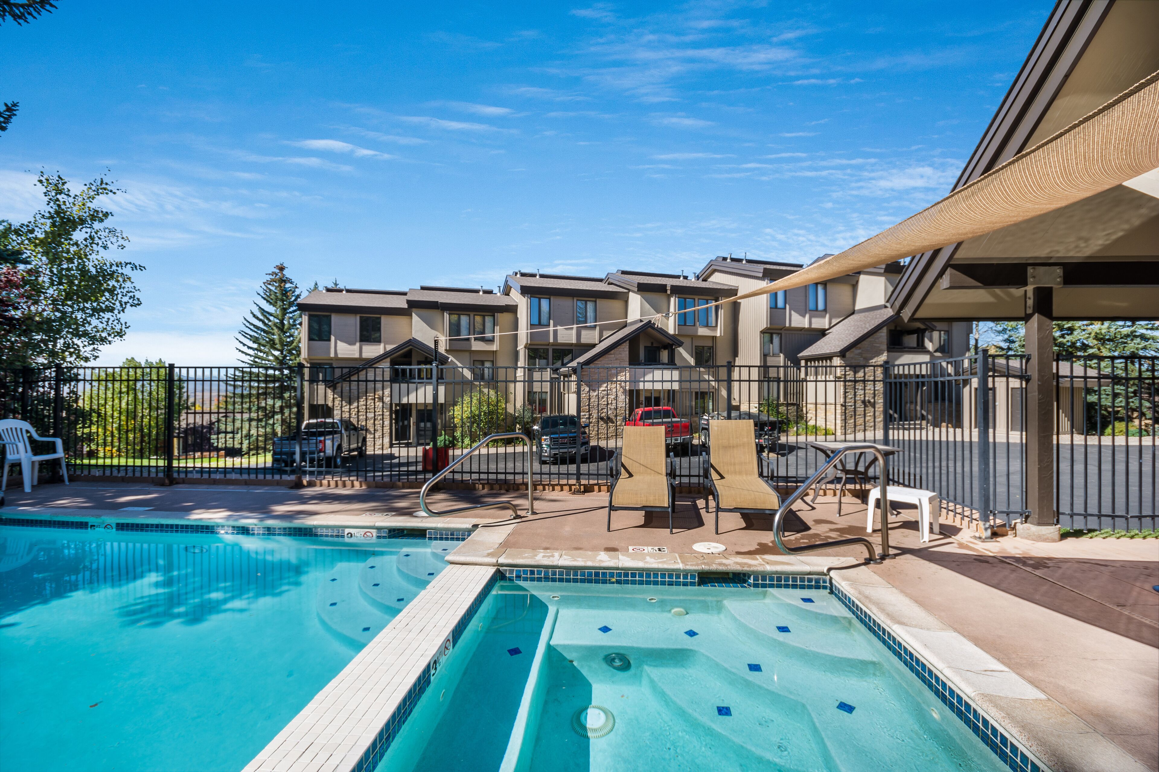 A swimming pool with lounge chairs and a covered area, surrounded by apartment buildings.