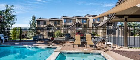 A swimming pool with lounge chairs and a covered area, surrounded by apartment buildings.