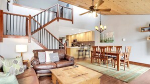 A spacious living area with a wooden staircase, a dining table with chairs, and a kitchen in the background. - Pool & Hot Tub | Deck with Views | Large Kitchen (Steamboat Springs)