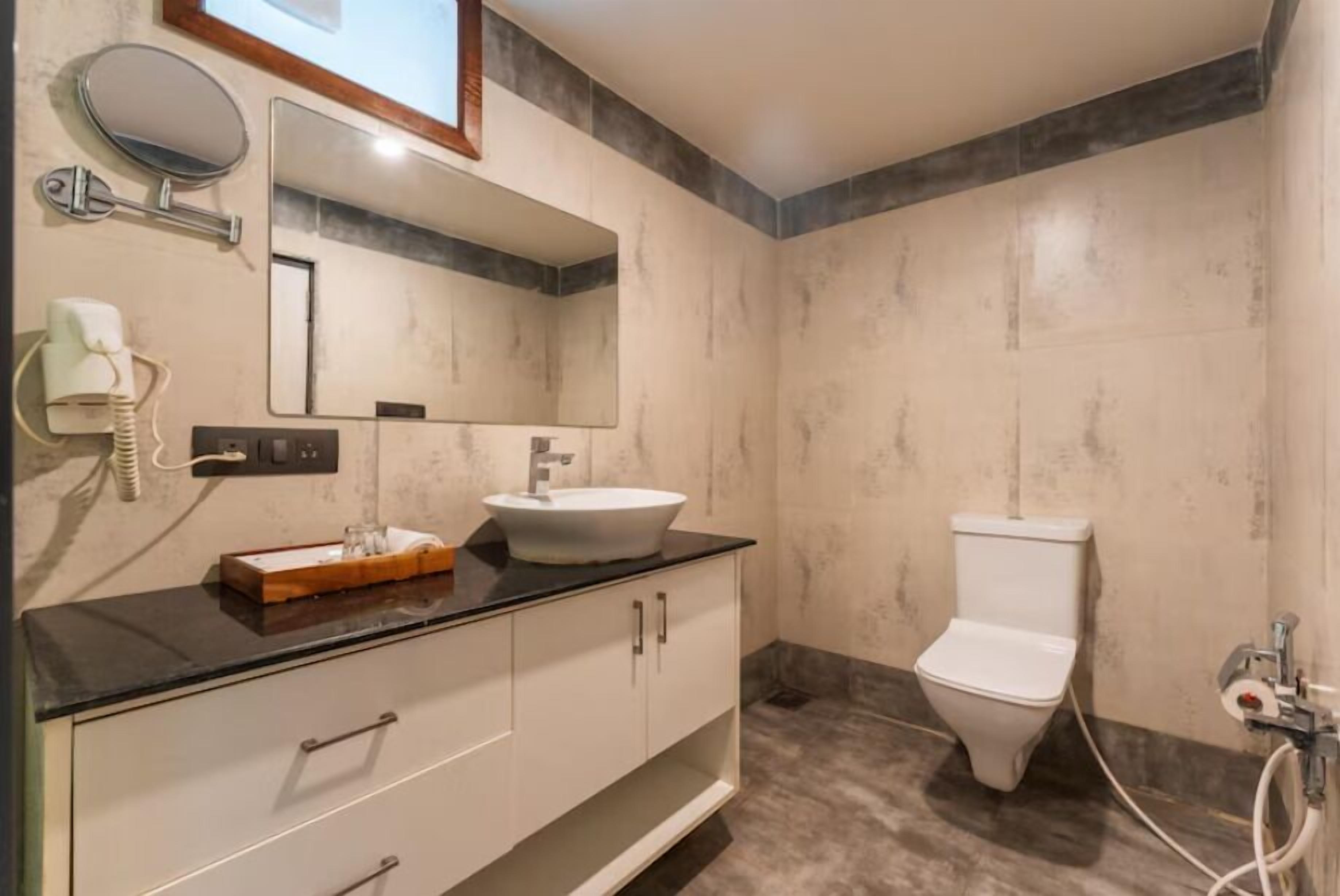 Un baño con lavamanos blanco, un espejo, inodoro y tocador con cajones.