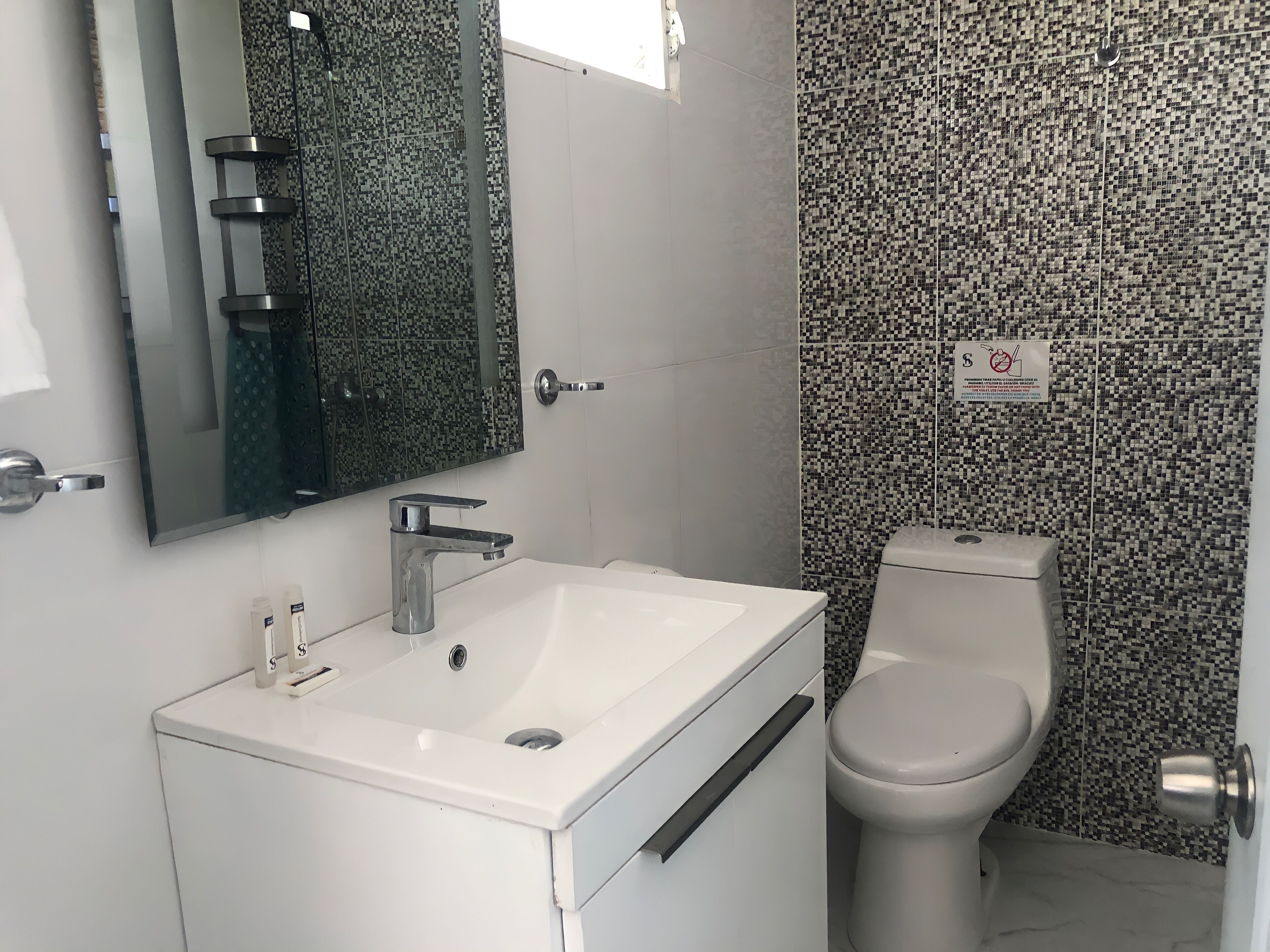 A bathroom with a white sink, a mirror, a toilet, and a tiled wall.