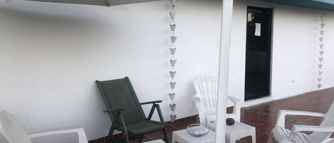A patio area with white plastic chairs and a table, an umbrella, and a green chair.