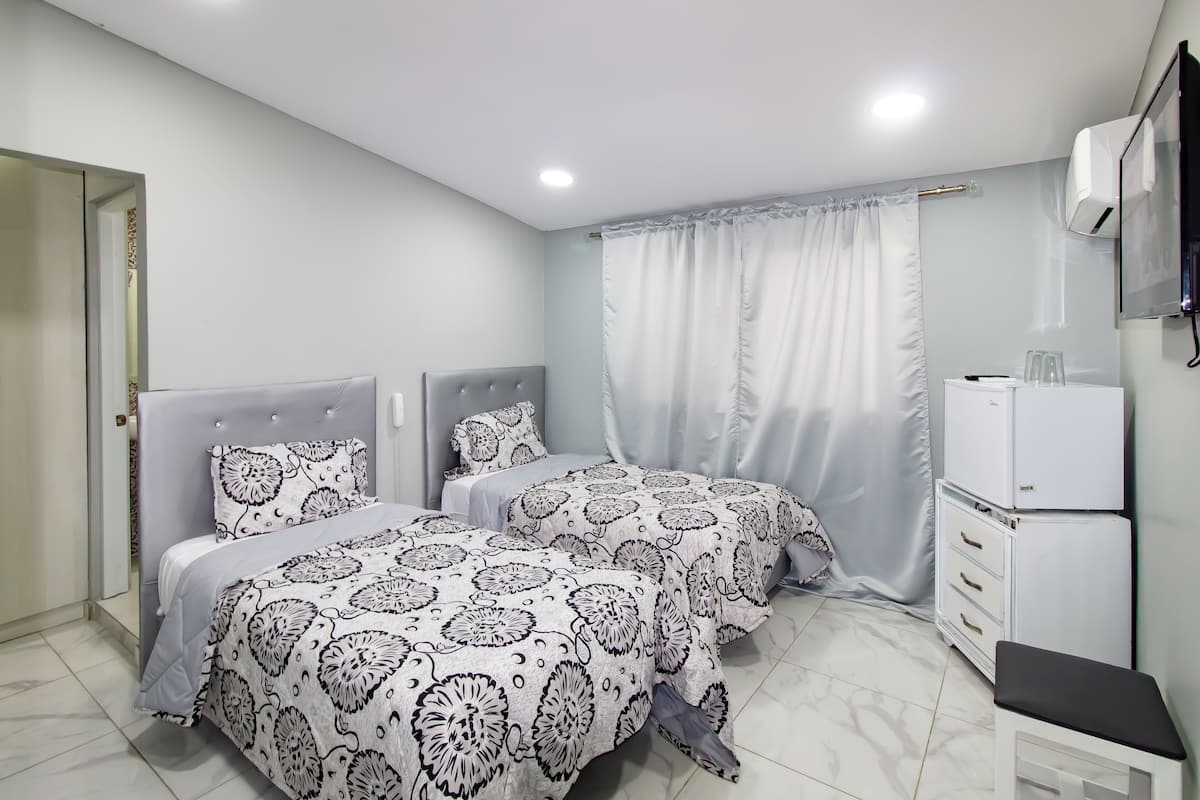 A bedroom with two beds, a wardrobe, a small table, and a TV.