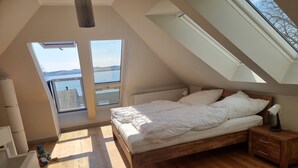 Camera da letto con un letto in legno, un comodino, una lampada e vista sull'esterno tramite finestre sul tetto.