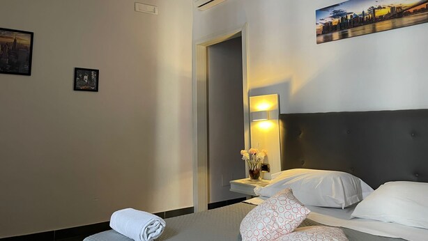 A hotel room with a bed, a nightstand, a wall-mounted air conditioner, a painting, and a framed picture. - Hotel Oceania (Naples)