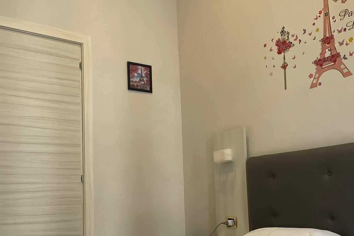 A hotel room with a bed, a white towel, a pink pillow, and a wall decoration of the Eiffel Tower.