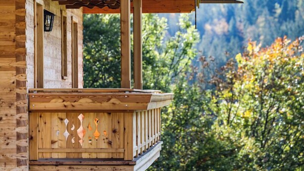 A wooden cabin with a balcony, a lantern, and a view of trees and mountains.