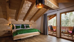 A wooden bedroom with a bed, a nightstand, and a window overlooking a deck.