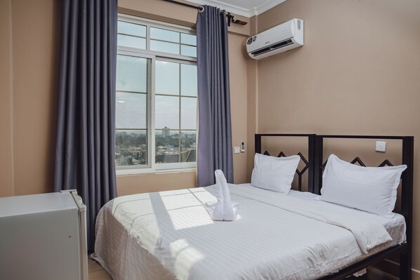 Quarto de hotel com cama, janela com cortinas, ar condicionado e vista para a cidade.
