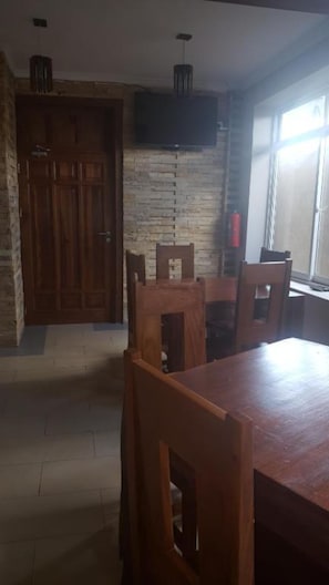 A dining area with a wooden table and chairs, a stone wall, and a flat-screen TV mounted above the table. - BML Highway Hotel (Dar es Salaam)