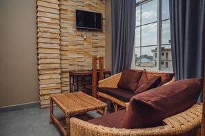 A cozy room with wicker furniture, a flat-screen TV on a stone wall, and a view through a window. - BML Highway Hotel (Dar es Salaam)