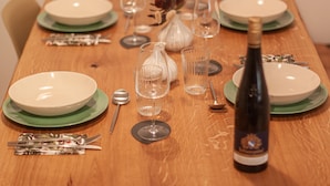 Ein Holztisch ist gedeckt mit Tellern, Besteck, Gläsern und einer Weinflasche.