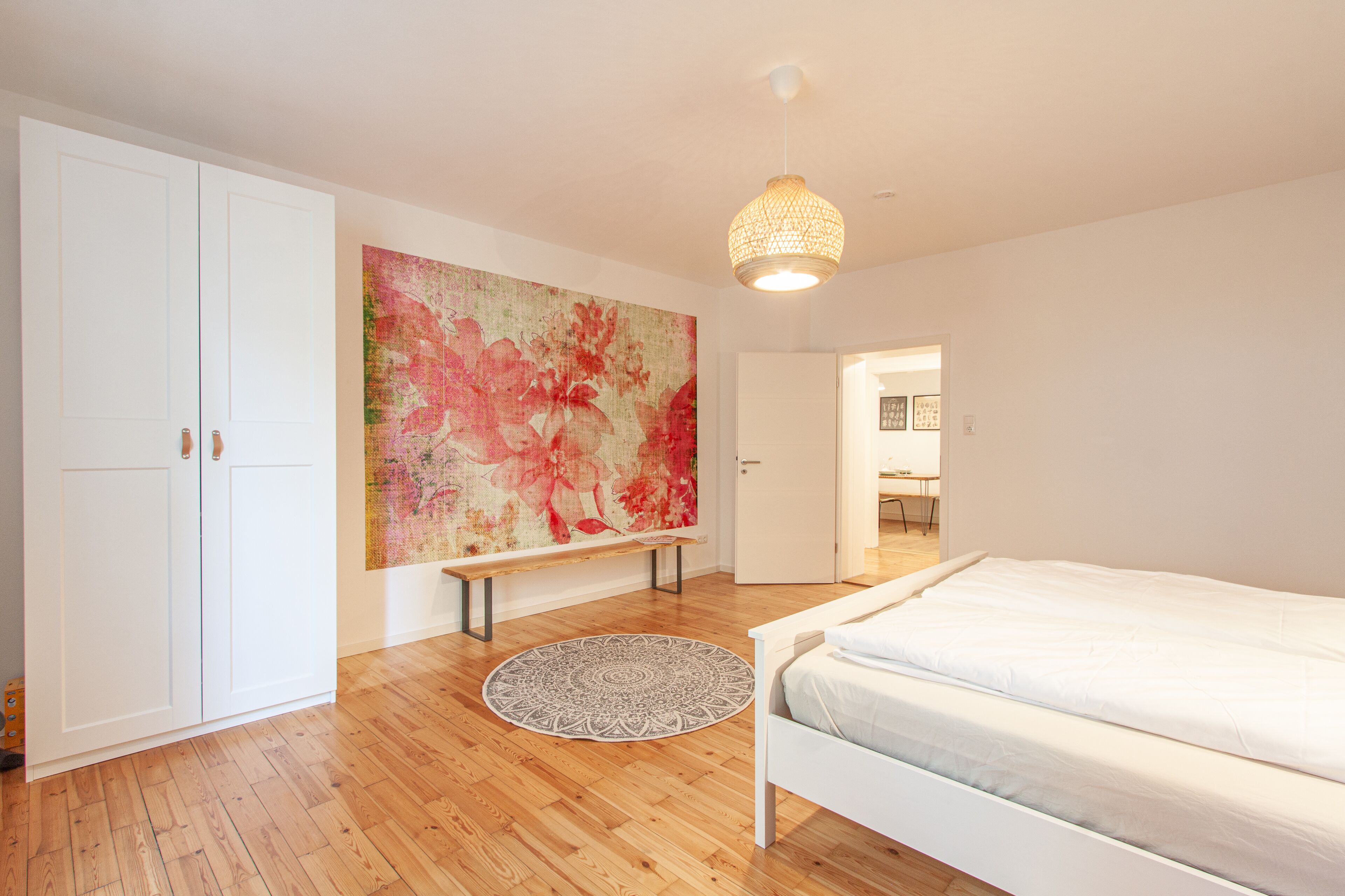 Une chambre à coucher avec un lit, un tapis rond, un banc et un grand tableau abstrait accroché au mur.