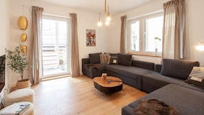 Ein modernes Wohnzimmer mit einem grauen Sofa, einem Holztisch und einem großen Fenster mit Vorhängen.