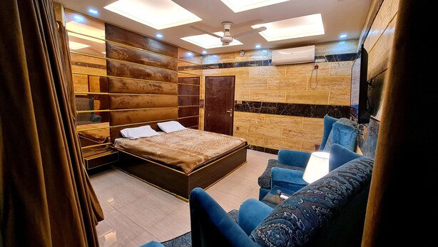 A modern bedroom with a bed, a seating area with chairs, a ceiling fan, and an air conditioning unit. - Smart Apartments & Hotel (Lahore)