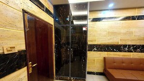 A lobby with a wooden wall, a dark wooden door, a black marble wall, a brown leather sofa, and a tiled floor. - Smart Apartments & Hotel (Lahore)