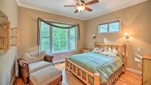 Ein Schlafzimmer mit einem hölzernen Bett, einem Sessel, einem Deckenventilator und zwei Fenstern.