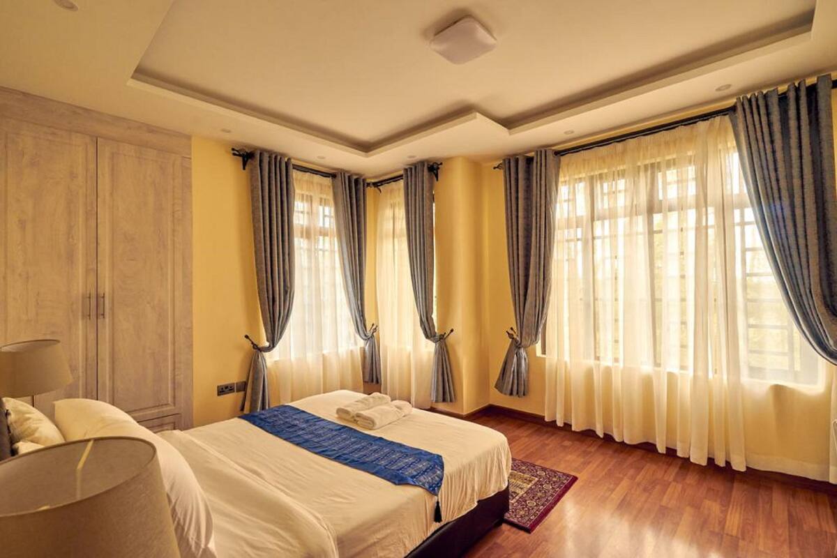 A hotel room with a large bed, a wooden wardrobe, and curtains on the windows.