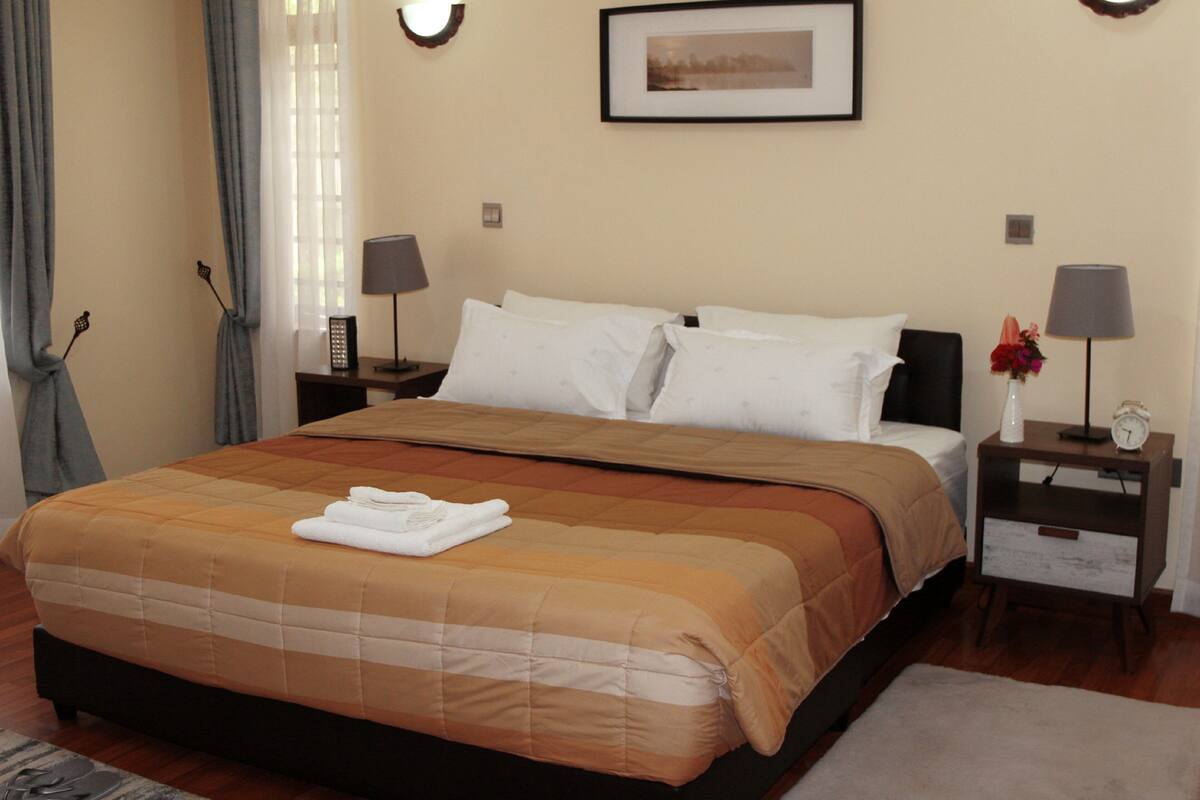A hotel room with a large bed, two bedside tables with lamps, a framed picture on the wall, and a window with curtains.