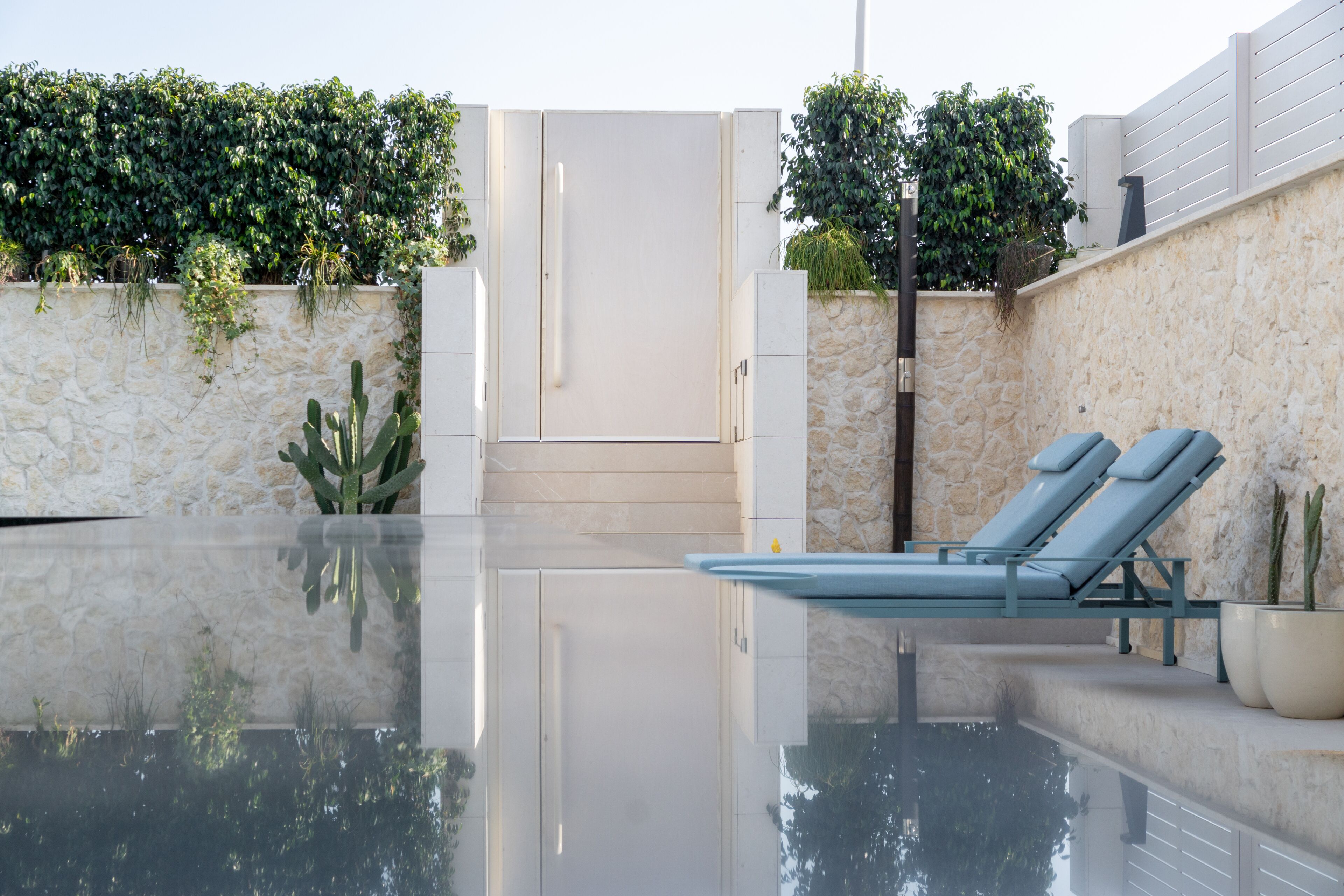 A modern outdoor pool area with a stone wall, a glass enclosure, and a lounge chair.