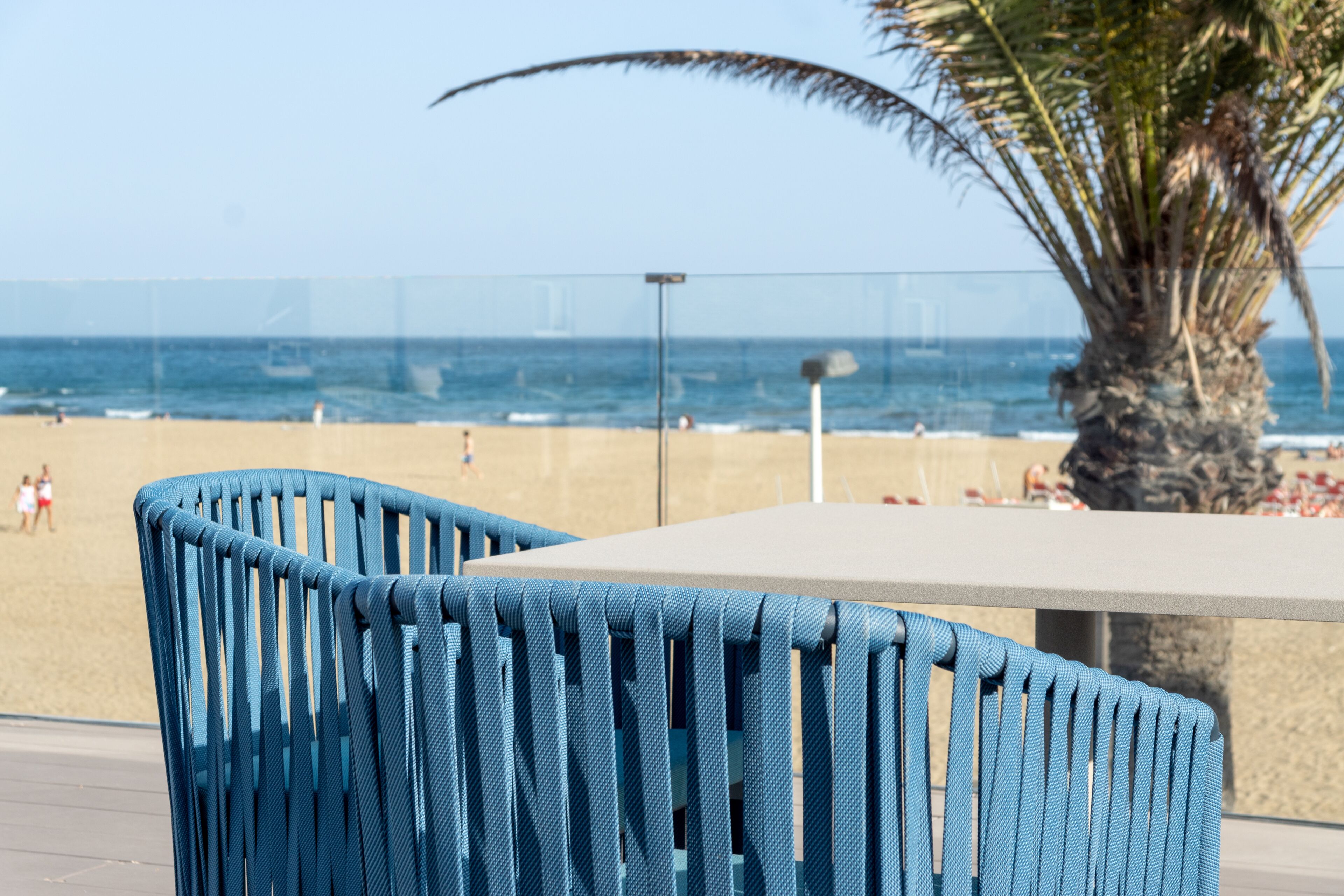 Una mesa junto a la playa con una silla azul, una palmera y vista al océano.