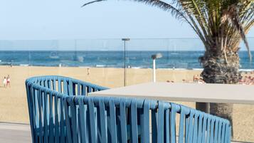 Una mesa junto a la playa con una silla azul, una palmera y vista al océano.