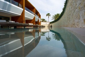 Un área de piscina moderna con vista despejada, sillones de descanso y una pared de piedra.