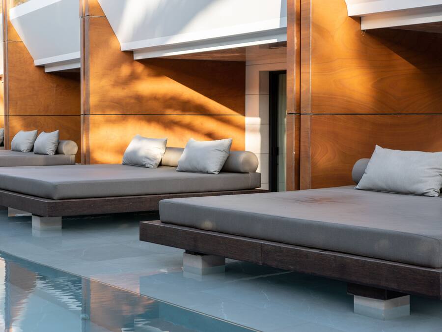 A modern poolside area with three sun loungers, each with cushions and a wooden base.