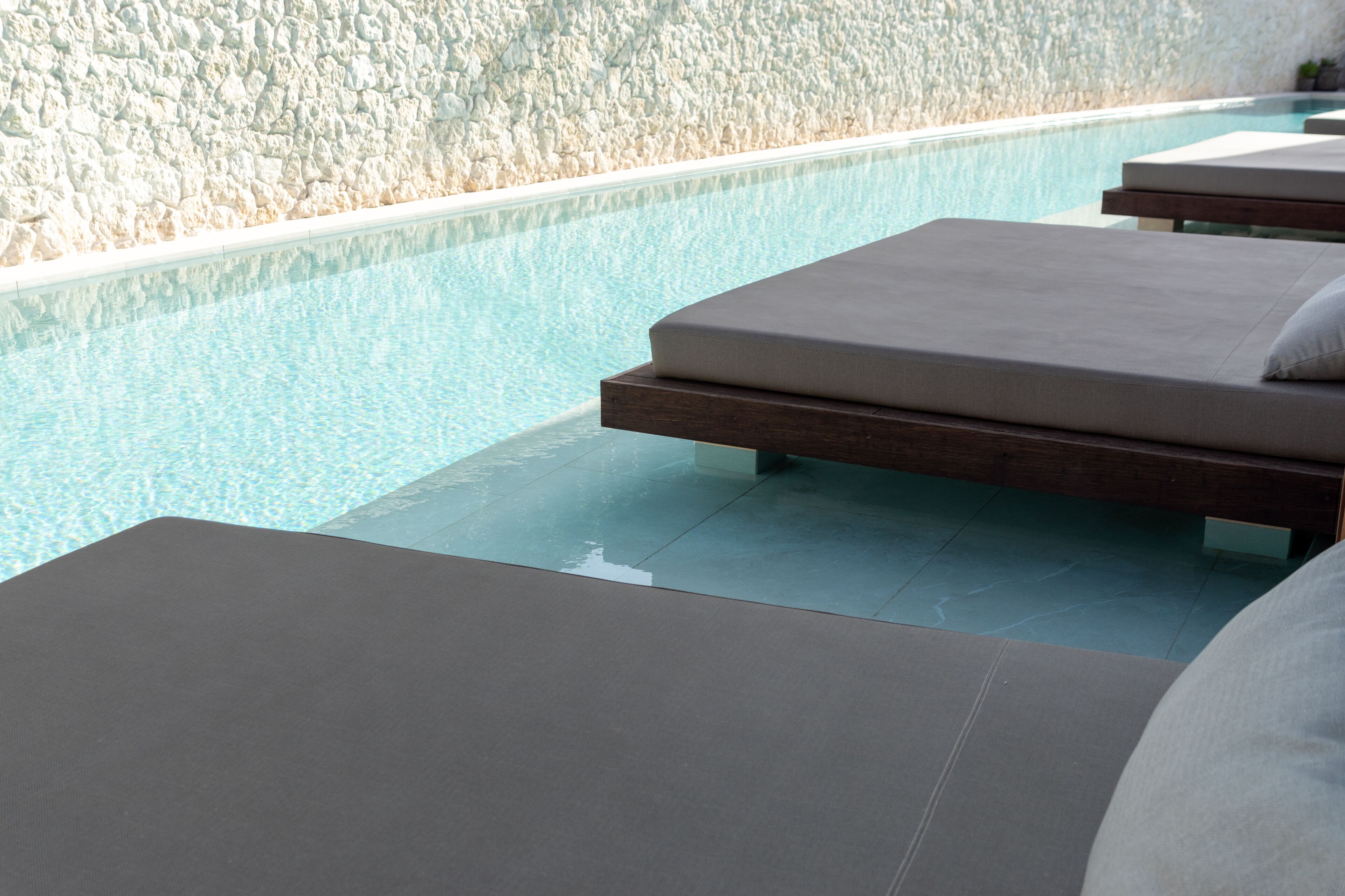 Un espace aménagé au bord de la piscine, avec des chaises longues et un mur à la texture granuleuse.