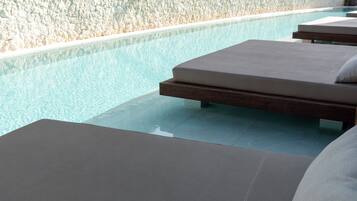 Un espace aménagé au bord de la piscine, avec des chaises longues et un mur à la texture granuleuse.