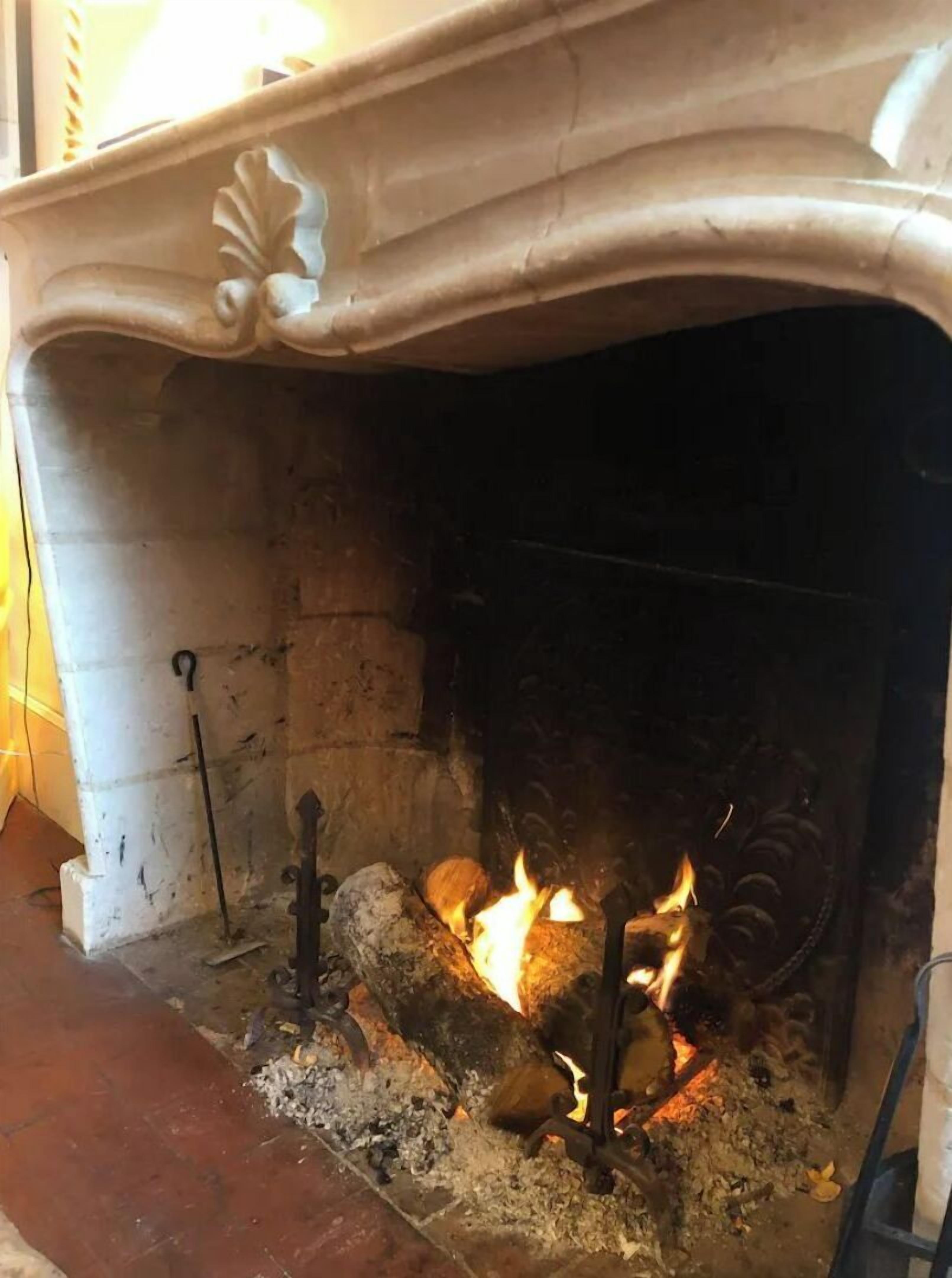 Une cheminée avec un manteau en pierre et une grille en métal.