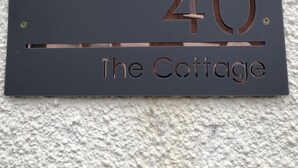 Eine Hausnummertafel mit der Aufschrift '40' und 'The Cottage' an einer strukturierten Wand.