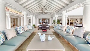 A spacious living area with a high ceiling and white columns, featuring a central seating area with sofas and a coffee table. - Villa Petite Plage 4 – Refined Beachfront Luxury in Grand Case, St. Martin (Grand Case)