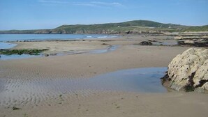 A sandy beach with a rocky outcrop and a hill in the background.
