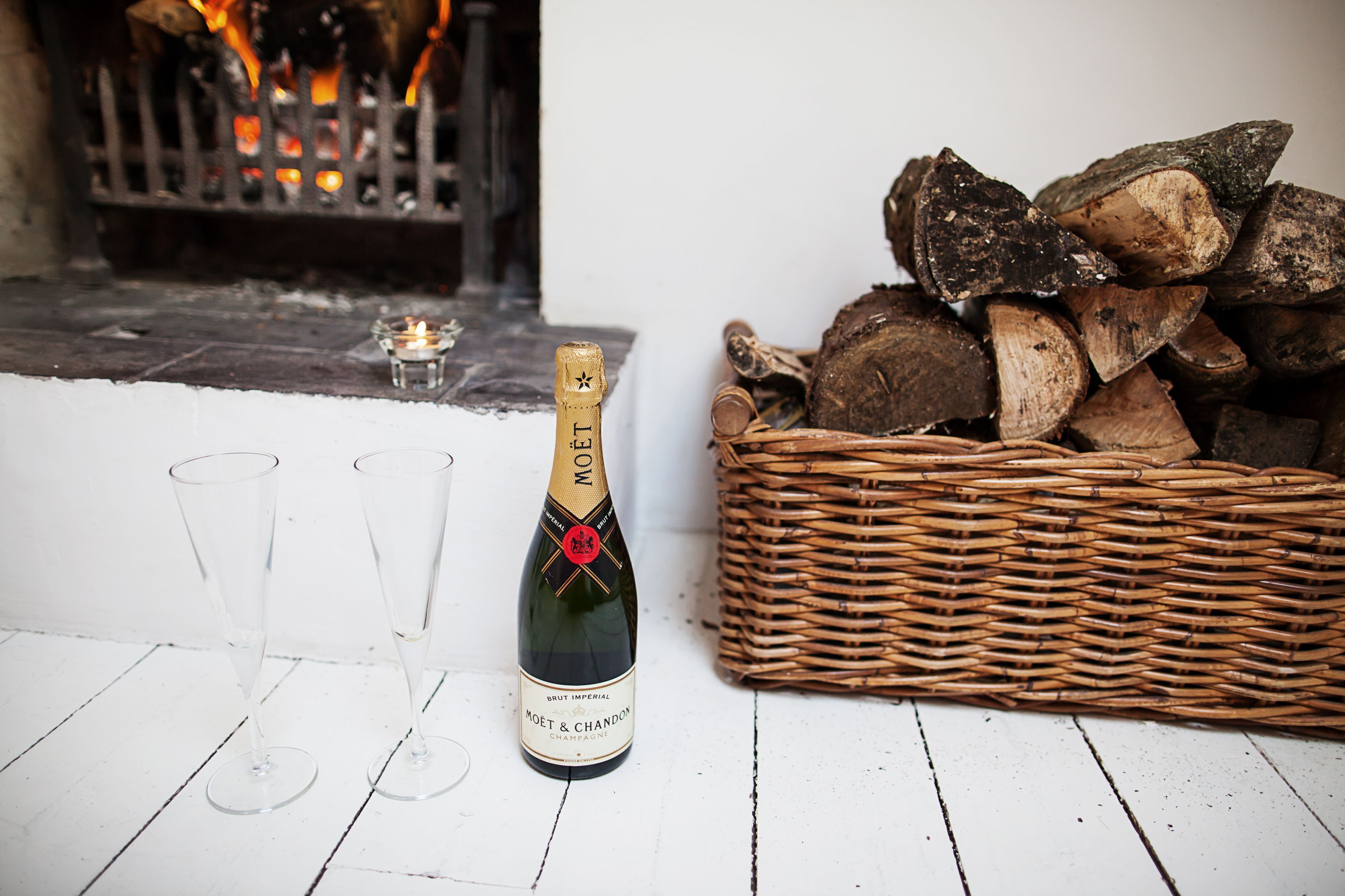 Pullo Moët & Chandon Brut Imperial -samppanjaa, kaksi tyhjää lasia ja punottu kori täynnä polttopuita.