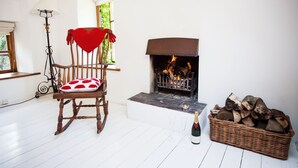 A cozy room with a fireplace, a rocking chair with a red cushion, a floor lamp, and a basket of firewood.