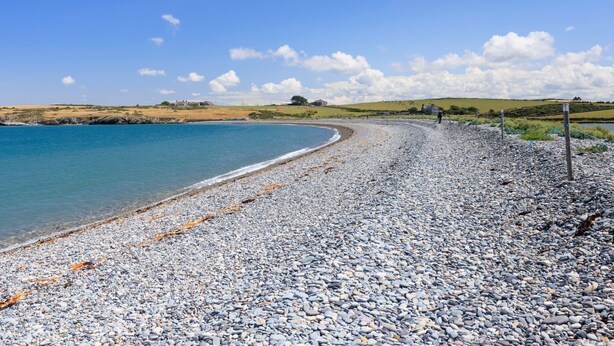 A pebbled beach with a clear blue sky and distant buildings. - Erw Rhys - sleeps 6 guests  in 3 bedrooms (Holyhead)
