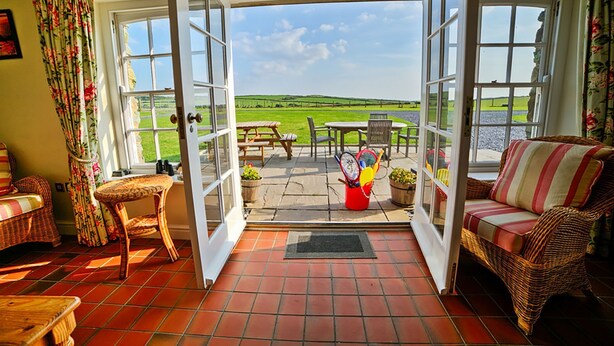 Ein Zimmer mit Blick auf ein grünes Feld, ein Korbssessel, ein kleiner Tisch und ein Stuhl.