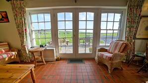 Ein gemütliches Zimmer mit Korbmöbeln, Fliesenboden und Blick durch eine Glasdoor auf eine Terrass.