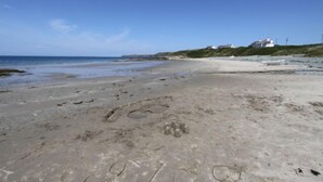 Ein Strand mit Fußspuren, einem Boot und Häusern im Hintergrund.