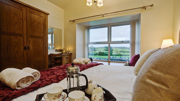 Habitación de hotel con una cama grande, una bandeja con juego de té, una ventana con vistas al campo y un armario de madera.