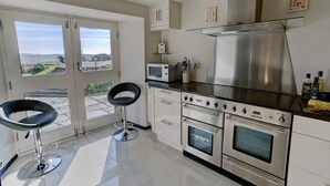 Una cuina moderna amb electrodomèstics d'acer inoxidable, un microones i un forn gran. Hi ha dos tamborets negres i una finestra amb vista al camp.