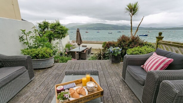 Un patio con muebles de mimbre, una bandeja con croissants, una bebida y vistas a barcos en el agua.