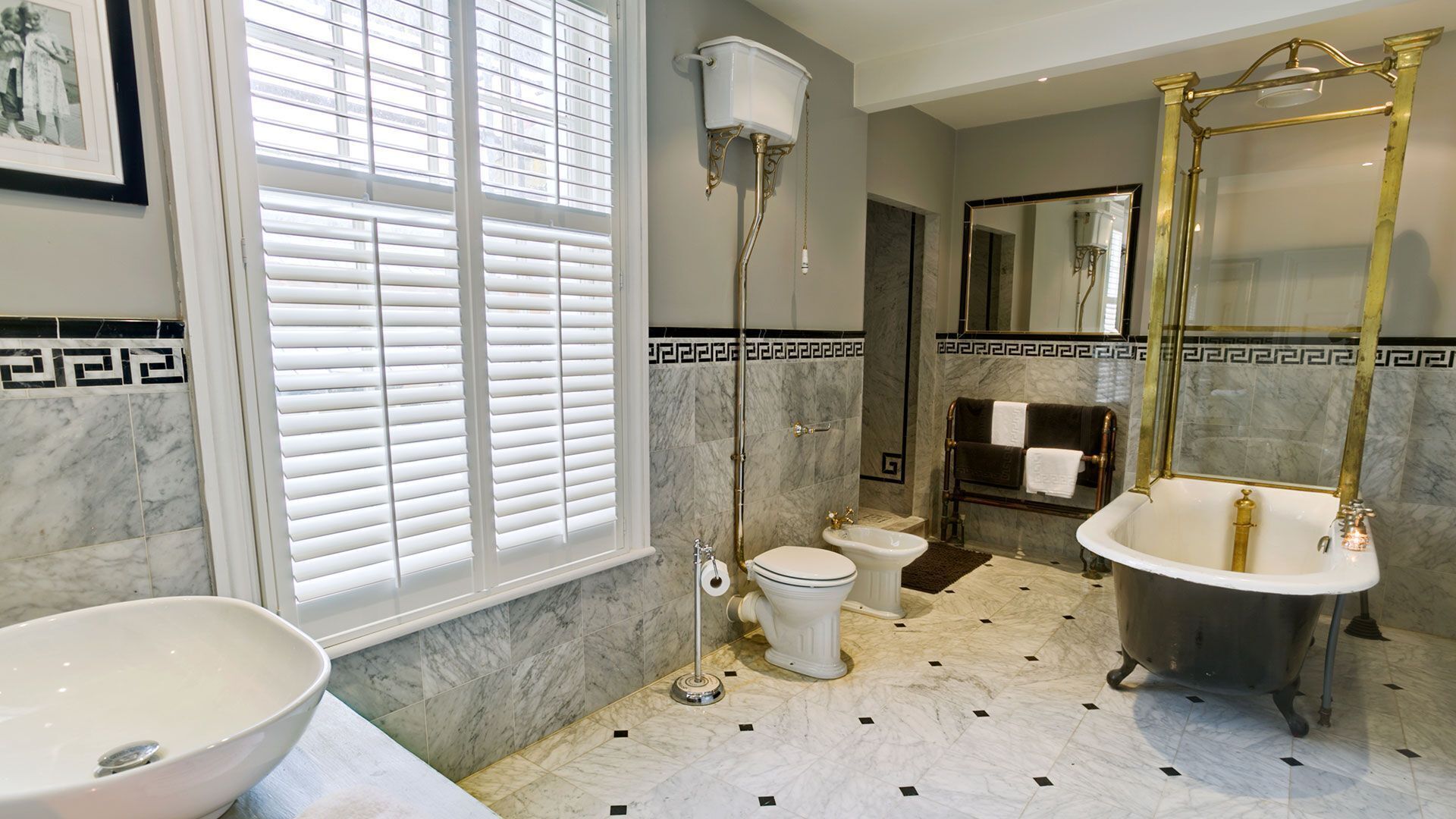 A bathroom with a large window, a freestanding toilet, a bidet, a bathtub, and a vanity with a bowl sink.