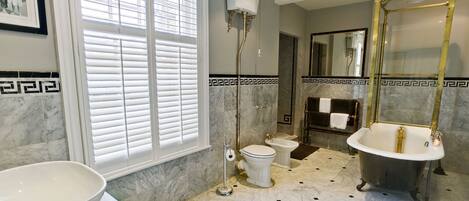 A bathroom with a large window, a freestanding toilet, a bidet, a bathtub, and a vanity with a bowl sink.