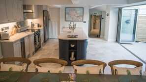 Cocina moderna con una isla central, zona de comedor con sillas y vistas al exterior.